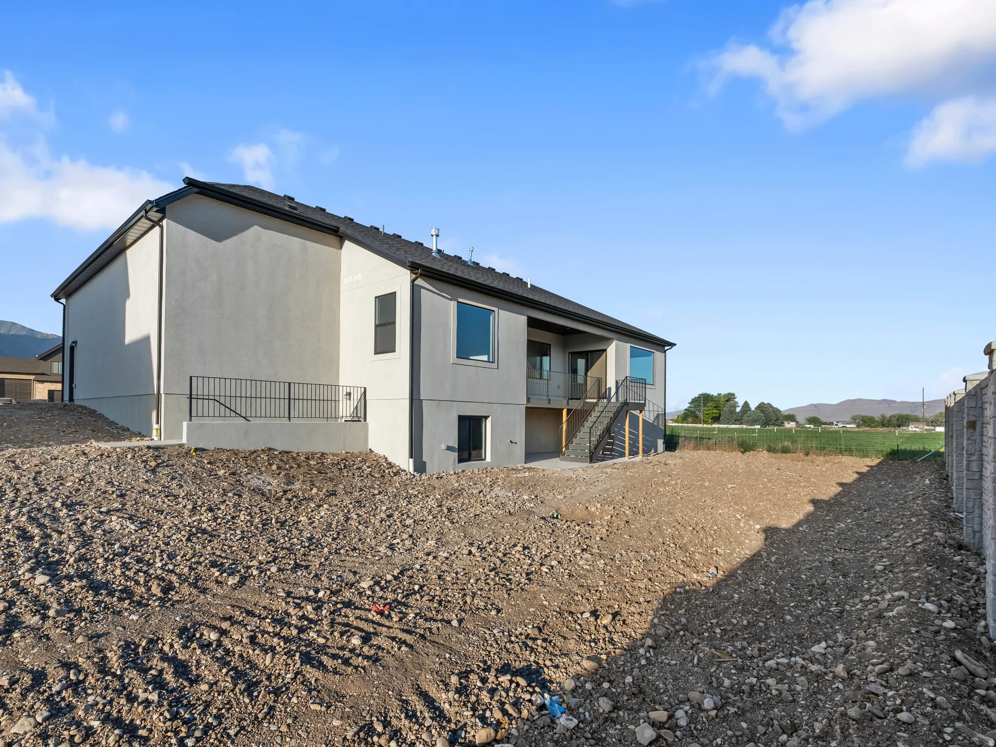 Stucco exterior, multi-story structure, black roof, ground-level patio with black railings, and an exterior staircase