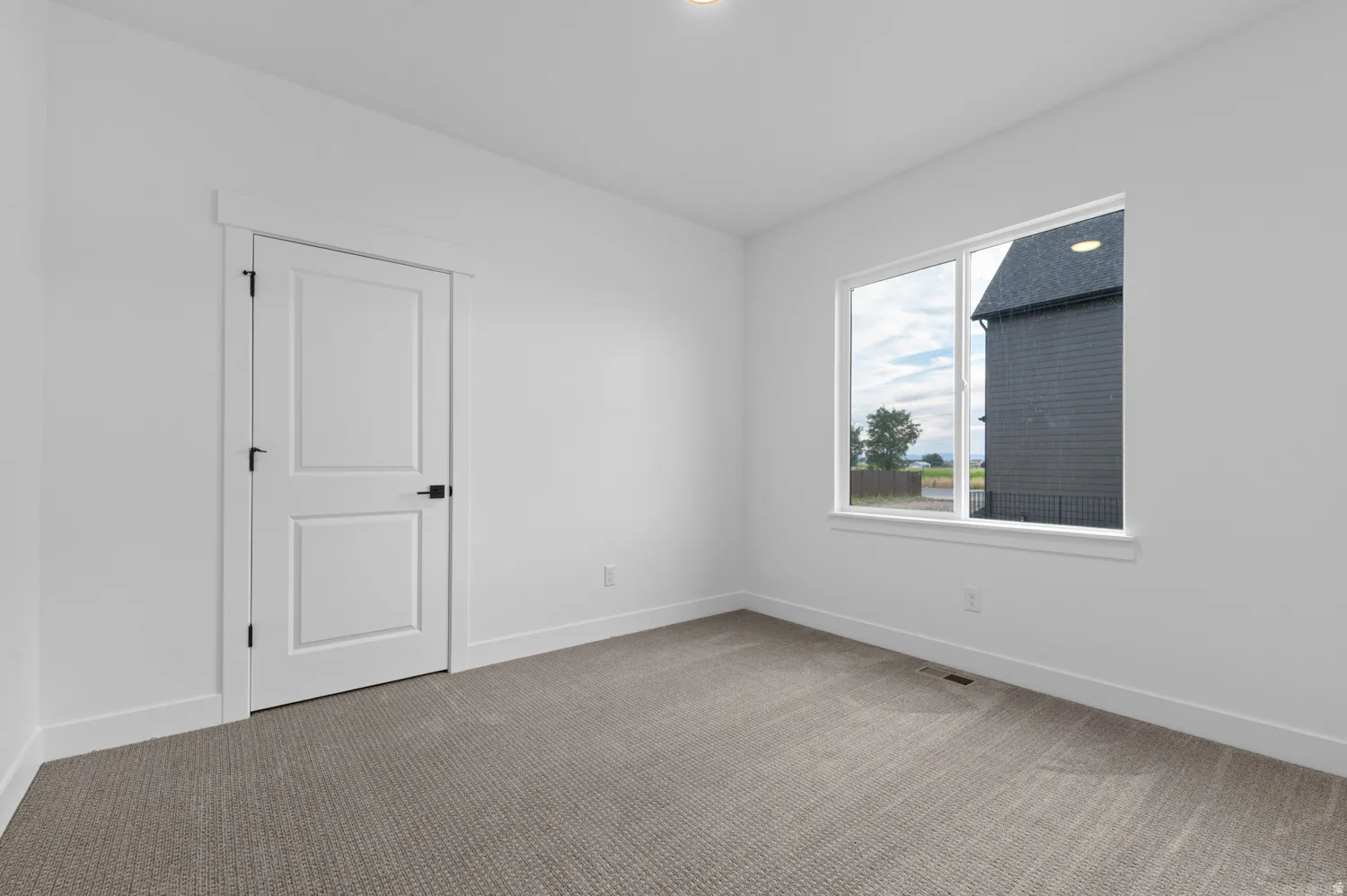 Neutral tone wall finish with a large window and grey carpet