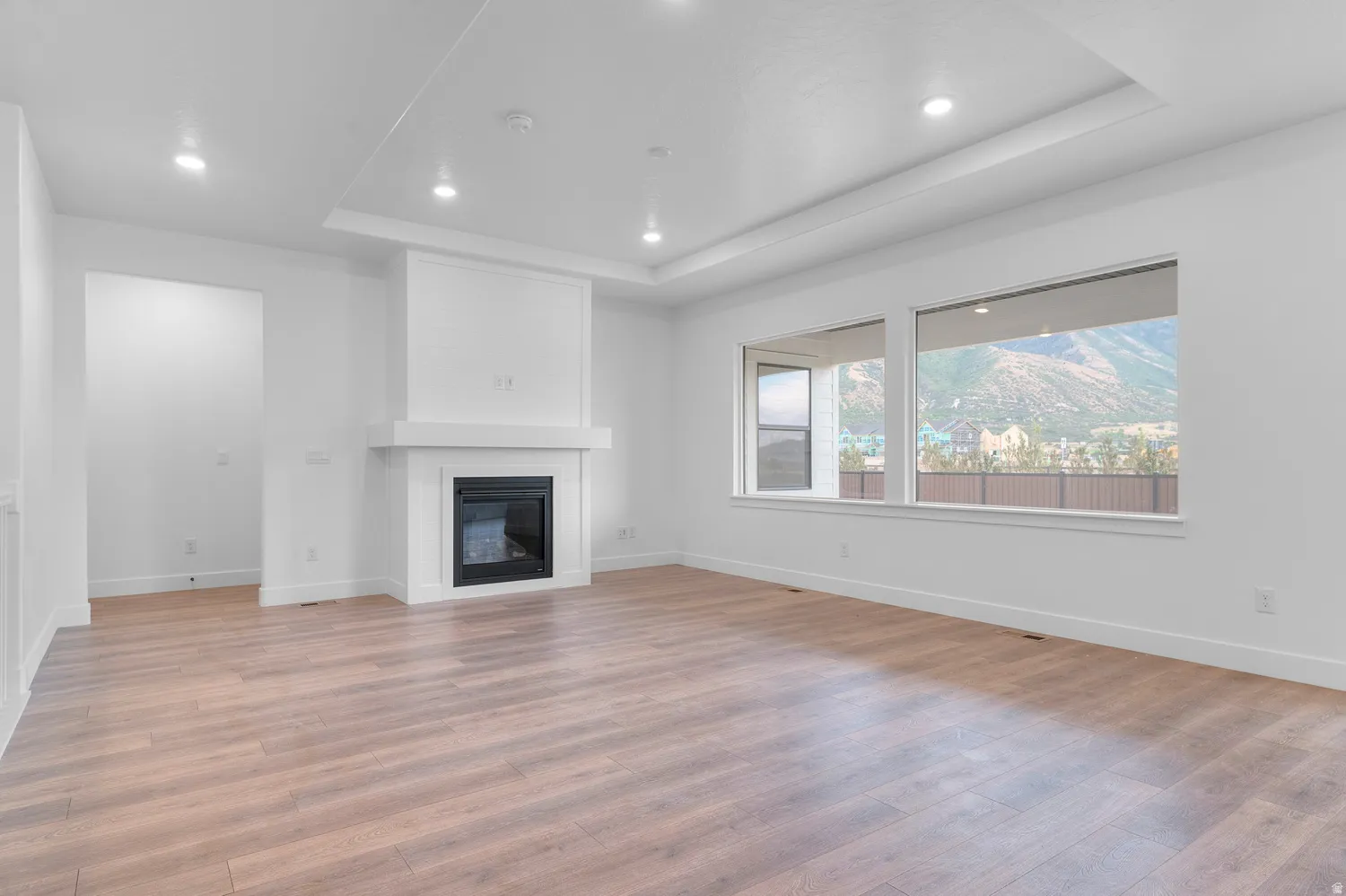 Recessed lighting, tray ceiling, integrated fireplace, expansive windows, and wood-finish flooring