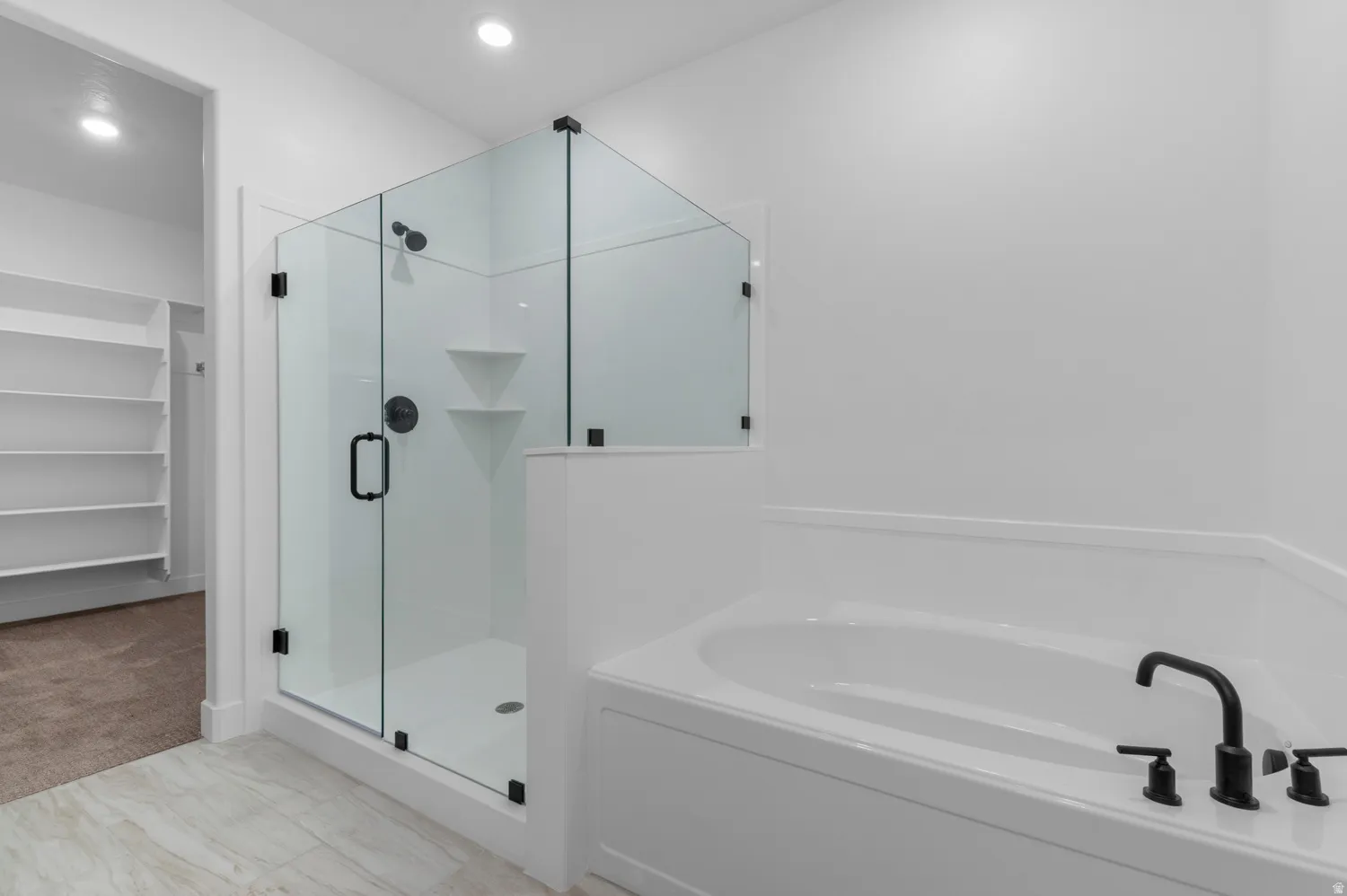 Glass-enclosed shower with matte black fixtures and built-in shelving, accompanied by a soaking tub with matching matte black faucet