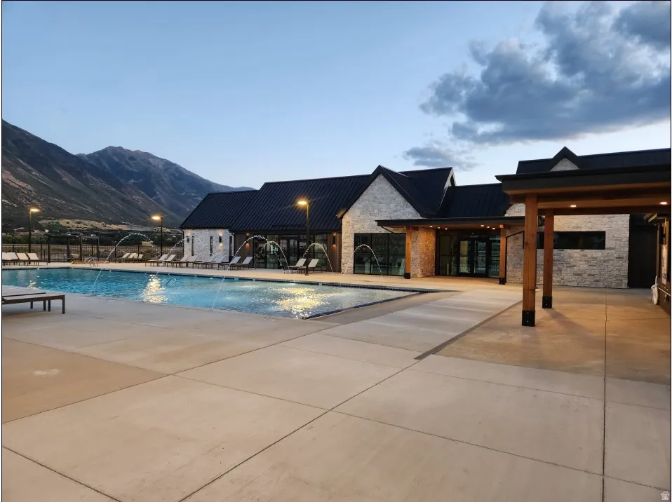 Outdoor swimming pool with integrated water features, expansive concrete decking, and mountain scenery