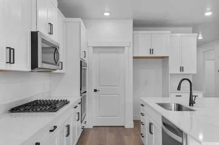 Modern kitchen featuring white cabinetry, stainless steel appliances, a gas cooktop, a built-in double oven, and wood-finish flooring