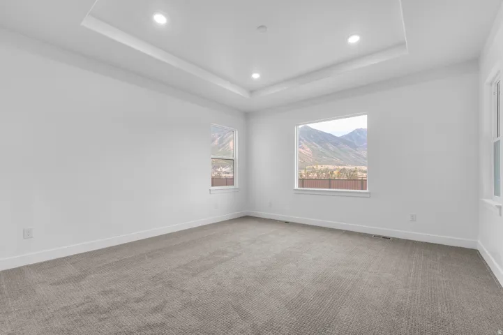 Tray ceiling with recessed lighting, neutral tone carpeting, white walls, and multiple windows