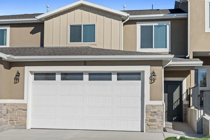Stucco exterior with stone veneer accents, white garage door with upper window panels, dark front entry door, and exterior sconce lighting