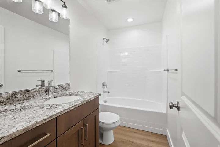 Bathroom featuring a dark wood-finish vanity, light-toned countertop, wood-finish flooring, and a white subway tile tub surround