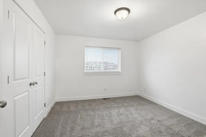 Plush carpet flooring, neutral wall tones, white trim, window with blinds, and ceiling-mounted lighting