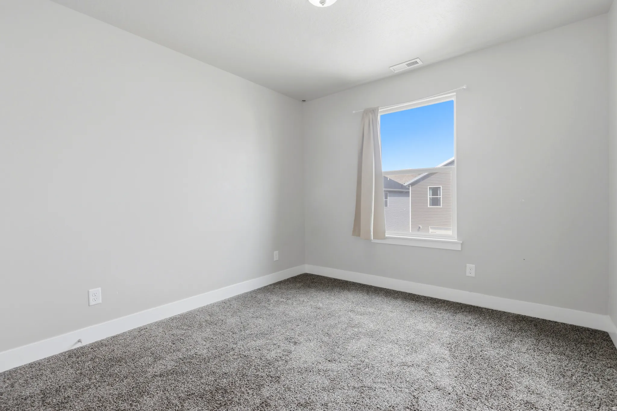 Spacious room featuring neutral carpeting, light gray wall tones, white trim, and a window with a curtain rod