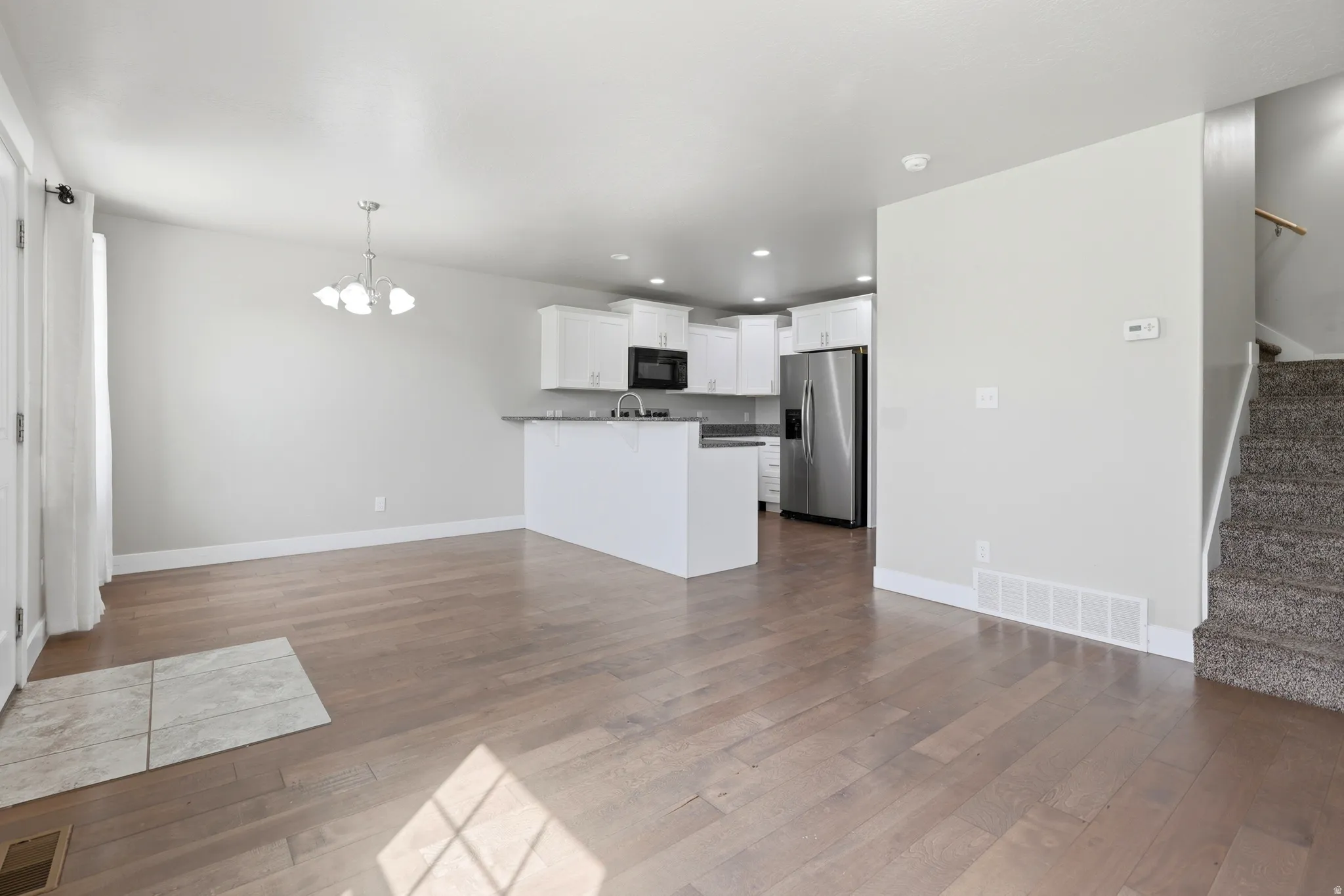 Open-concept living area with wood-finish flooring, white cabinetry, stainless steel appliances, and a carpeted staircase