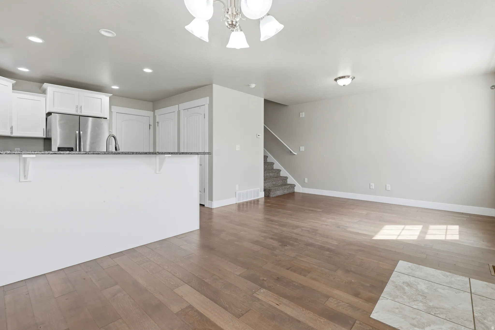 Kitchen island, stainless steel refrigerator, wood-finish flooring, white cabinetry, recessed lighting