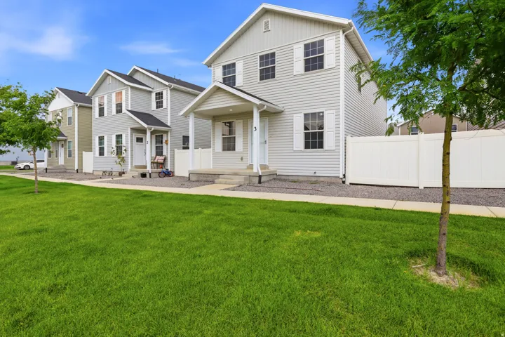 Two-story residence featuring light-colored siding, contrasting dark roof, white window shutters, a covered porch, and an enclosed backyard with a white privacy fence