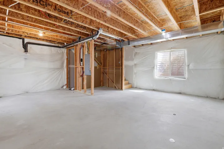 Unfinished concrete floor, exposed wood ceiling joists, visible electrical panel, and a small window