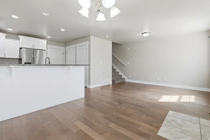 Kitchen island with a granite-style countertop, stainless steel refrigerator, white cabinetry, and wood-finish flooring