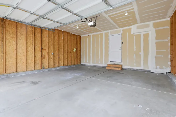 Concrete garage floor, exposed wood-frame wall, pre-hung white door, recessed ceiling lights, automatic garage door opener