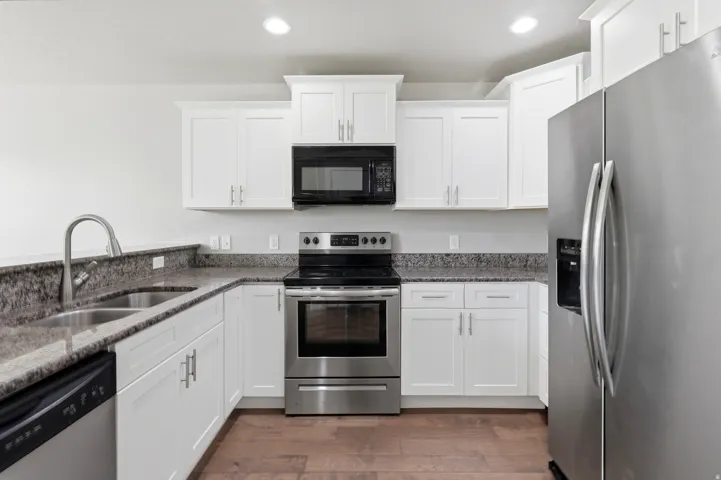 White cabinetry, stainless steel appliances, granite countertops, double basin sink, and wood-finish flooring