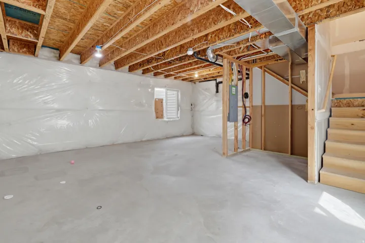 Unfinished basement featuring exposed wood joists, concrete flooring, and a framed utility area