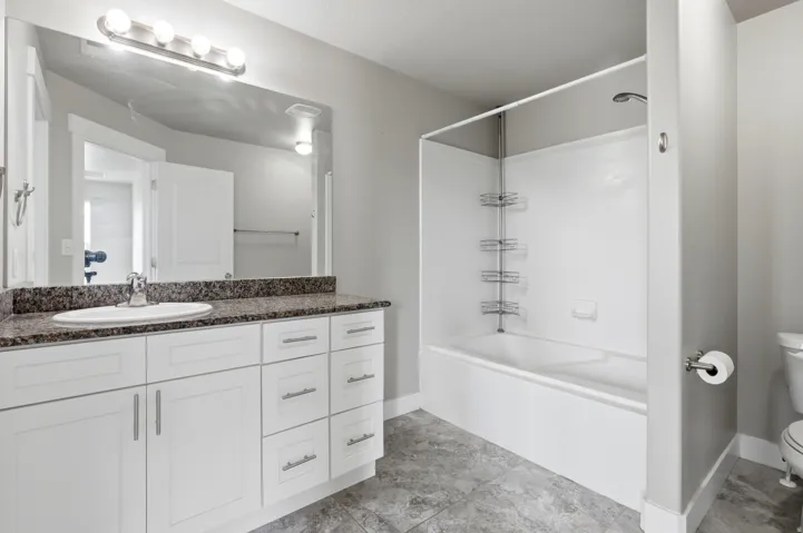 White vanity with extensive storage, granite-look countertop, integrated sink, and chrome faucet