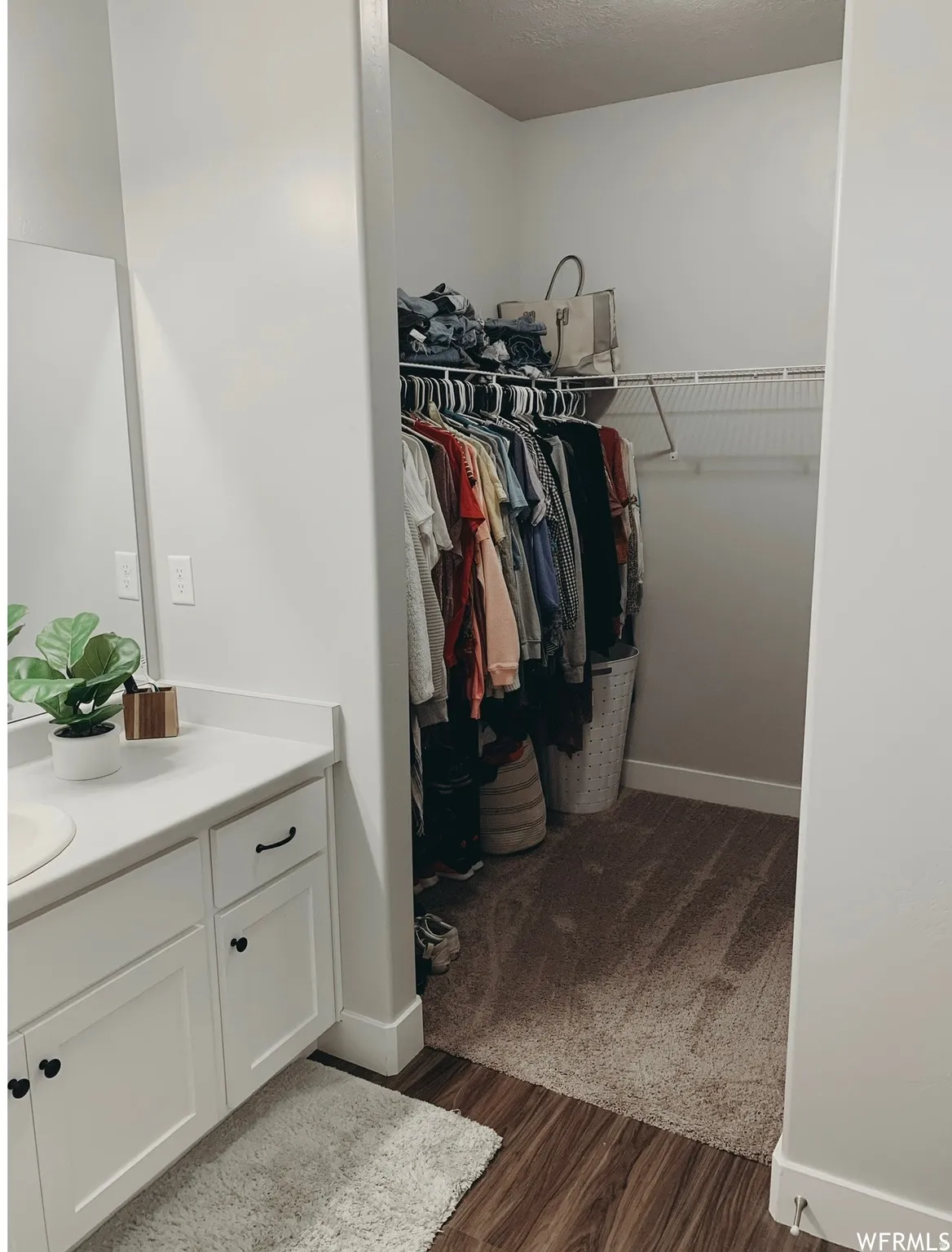 White cabinetry with black hardware, white countertop, walk-in closet with wire shelving, and wood-finish flooring