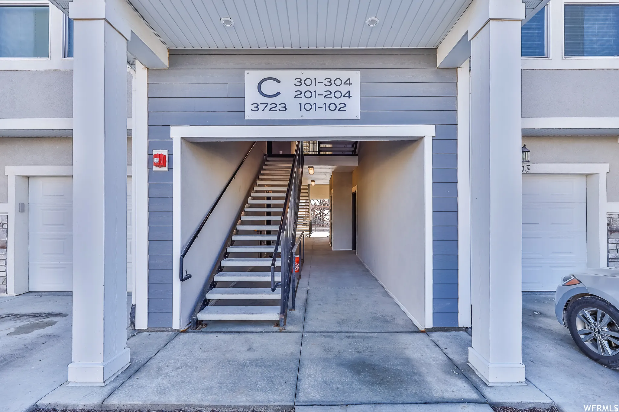 Exterior entrance featuring a prominent central staircase, gray siding, white trim, and integrated garage doors