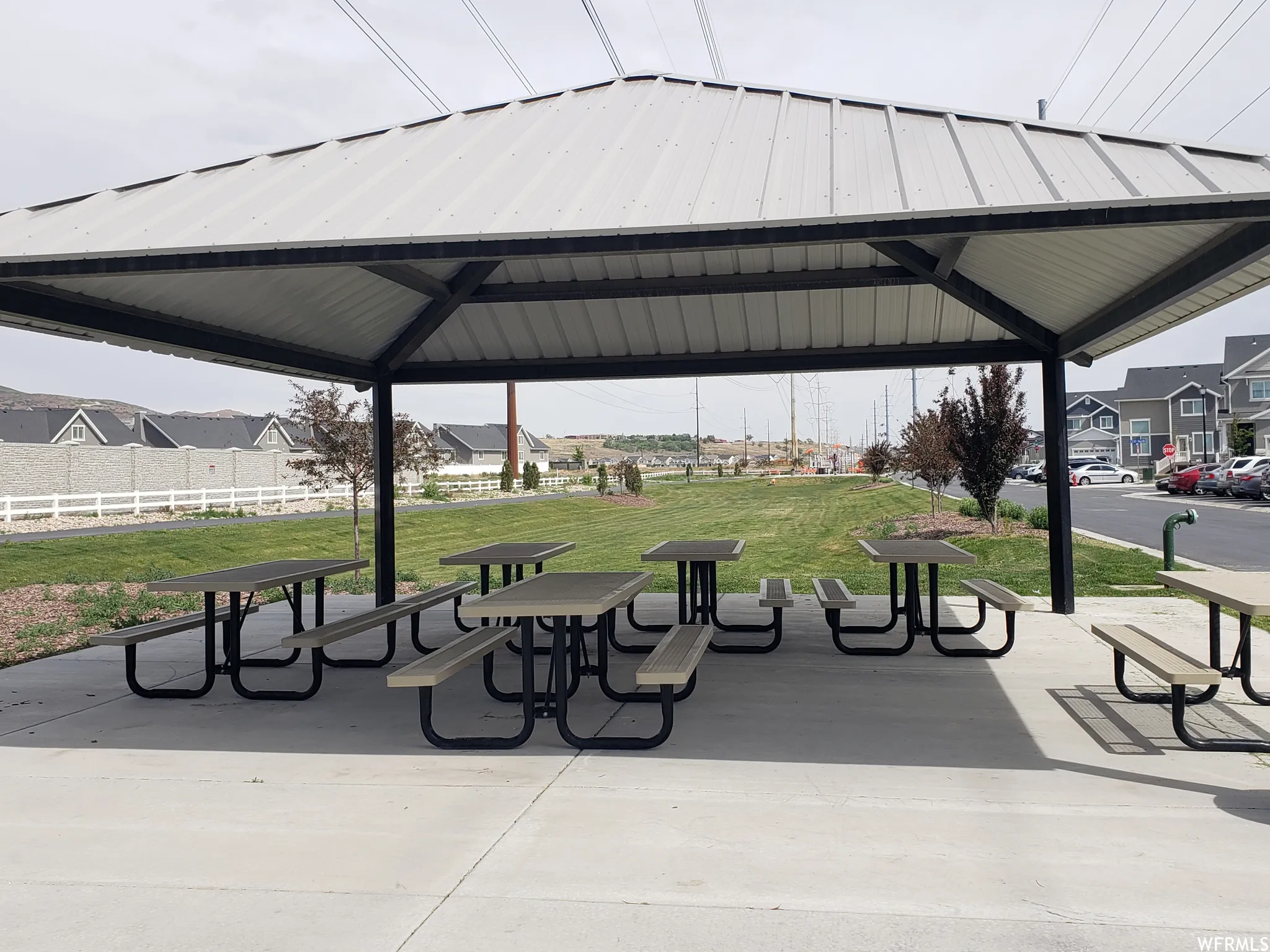 Sheltered outdoor gathering area featuring a metal roof structure, multiple picnic tables, and a concrete pad