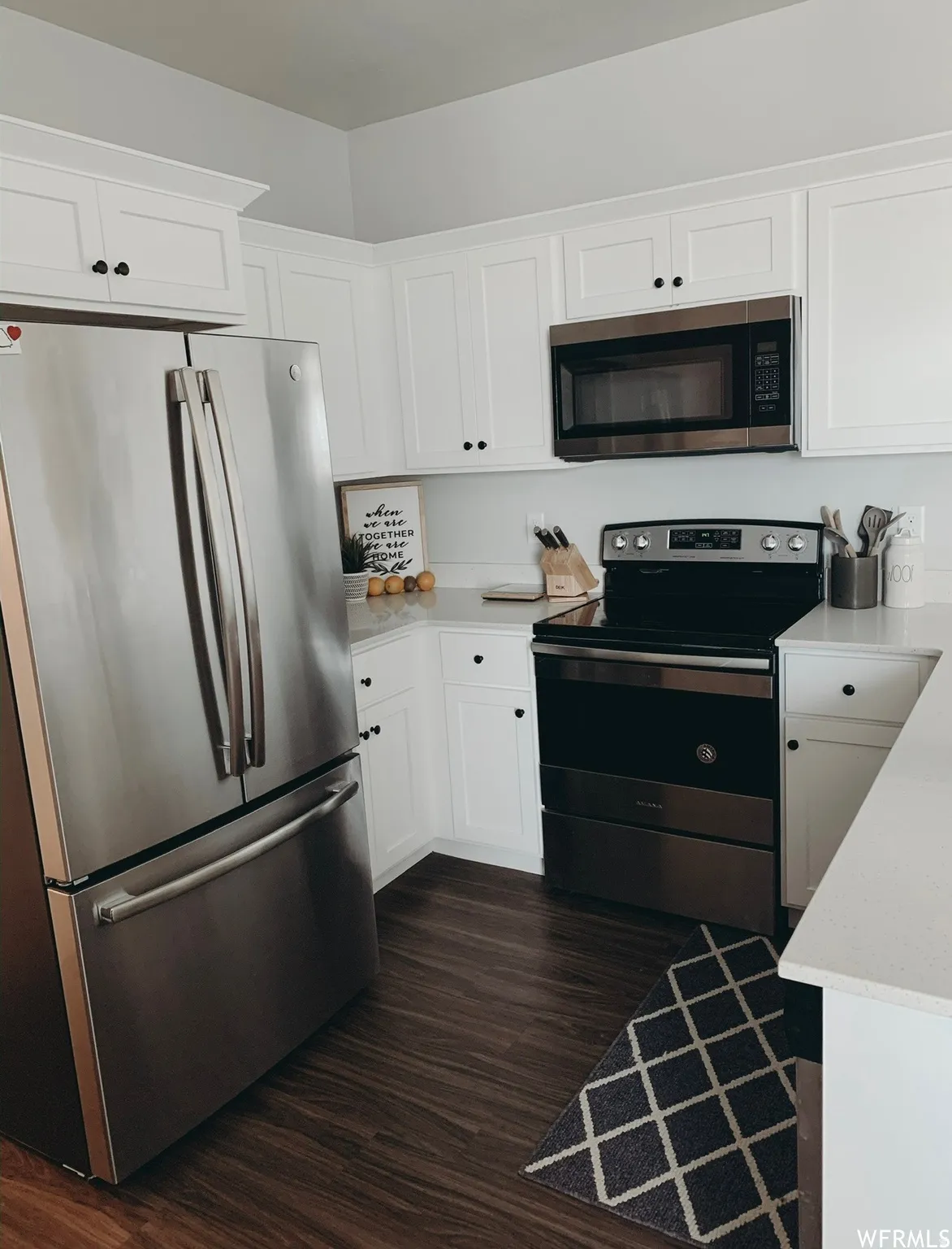 White cabinetry with black hardware, stainless steel refrigerator, stainless steel microwave, black range, wood-finish flooring