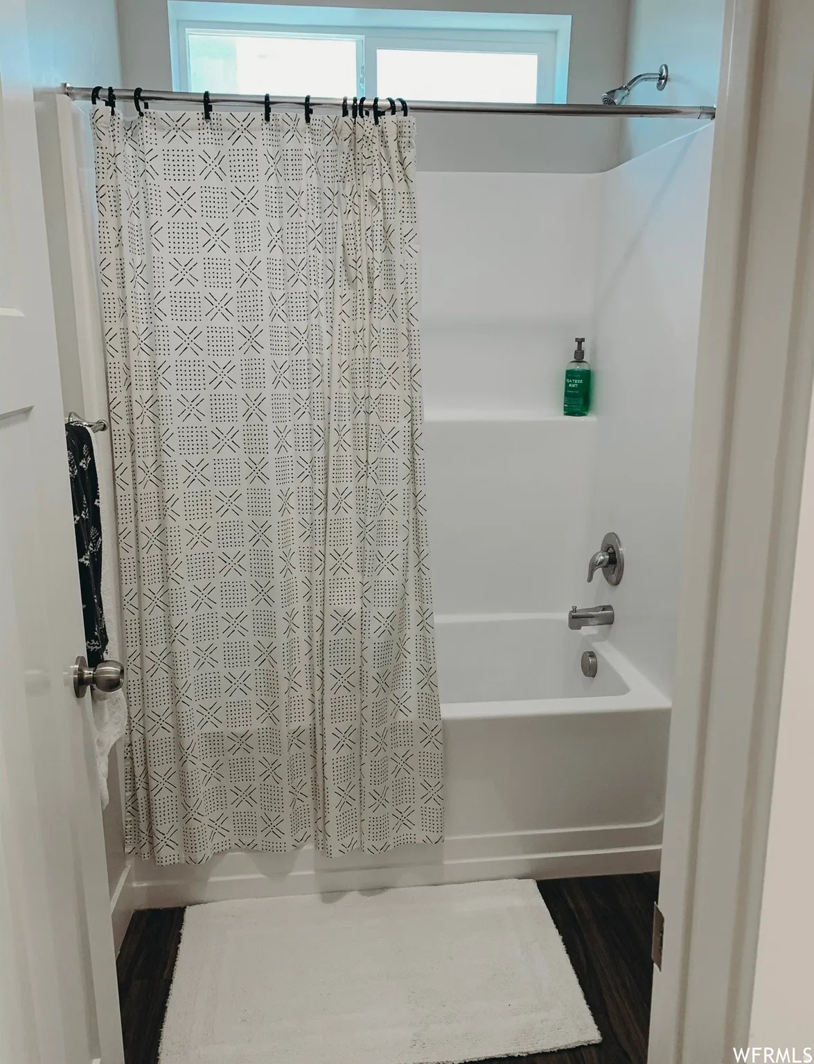Bathtub with integrated shower, chrome fixtures, and a high-set window