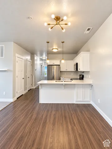 Open-concept living space featuring wood-finish flooring, a kitchen island with integrated sink, white cabinetry, stainless steel refrigerator, and recessed lighting