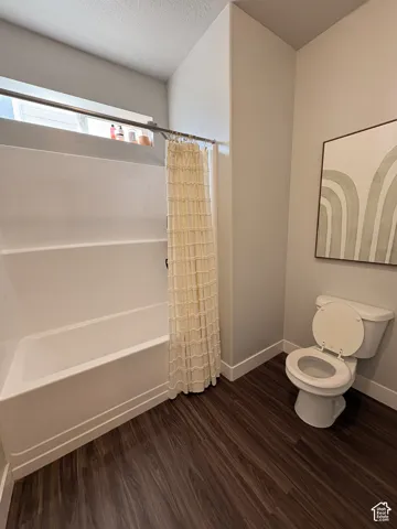 Full bathtub with shower, dark wood-finish flooring, and a white toilet