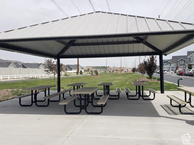 Sheltered outdoor gathering area featuring a metal roof structure, multiple picnic tables, and a concrete pad
