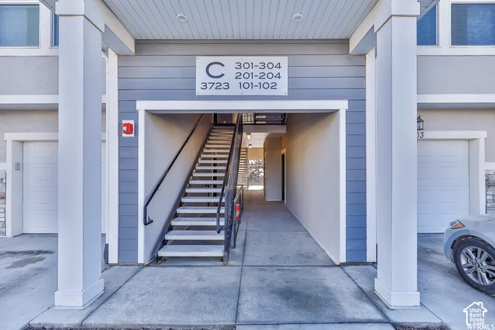 Exterior entrance featuring a prominent central staircase, gray siding, white trim, and integrated garage doors