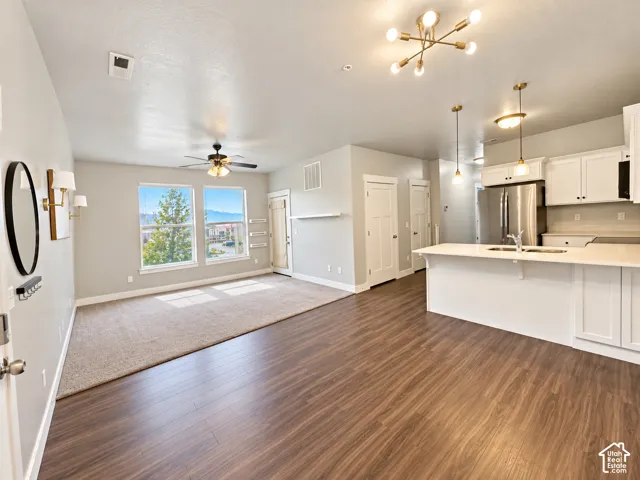 Open-concept living area with wood-finish flooring, white kitchen cabinetry, and an island with a sink