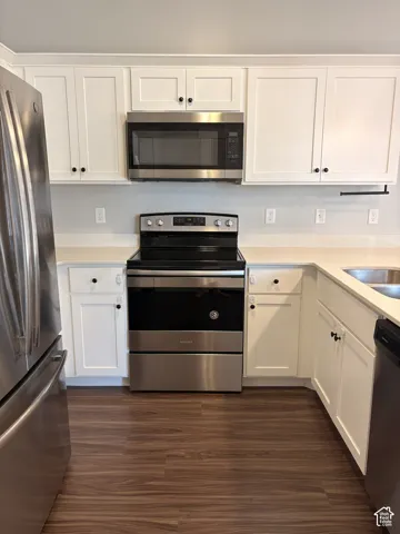 White shaker-style cabinetry with black hardware, stainless steel appliances, light-toned countertops, and wood-finish flooring