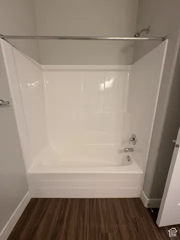 White fiberglass tub and shower combination with chrome fixtures and wood-finish flooring