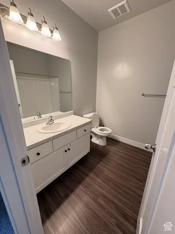 White vanity with integrated sink, wood-finish flooring, and wall-mounted light fixture
