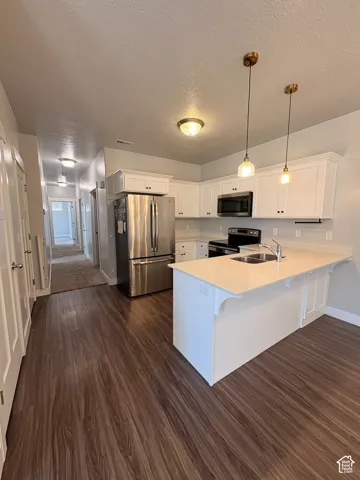 Kitchen featuring white cabinetry, stainless steel appliances, wood-finish flooring, a kitchen island with seating, and pendant lighting