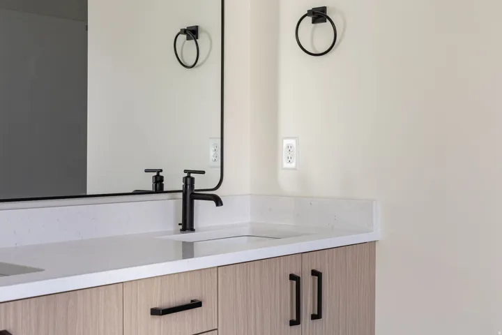Dual vanity with integrated sinks, light-toned wood-finish cabinetry, black hardware, and a framed mirror