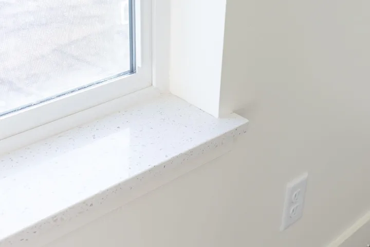 White window frame with a polished speckled sill, set against a light-toned wall