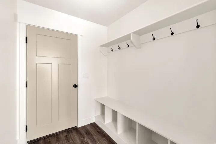 Wood-finish flooring, white panel door with black hardware, built-in bench with cubbies, and integrated shelving with black coat hooks