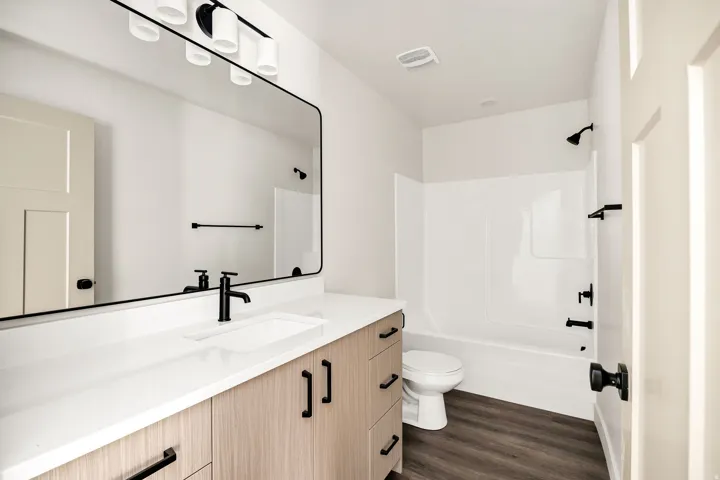 Bathroom featuring a wood-finish vanity with a white countertop, large wall-mounted mirror, and black fixtures