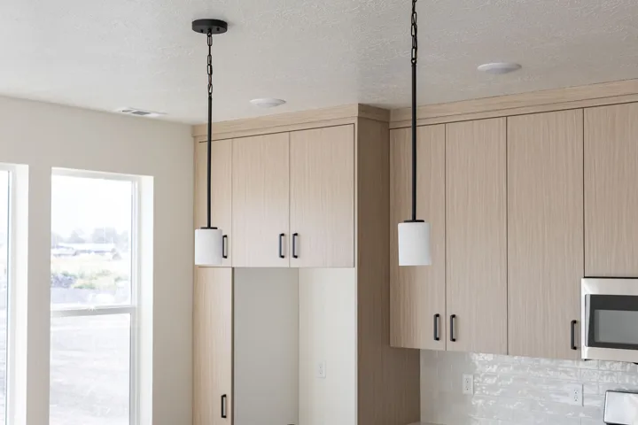 Light wood-finish cabinetry, contemporary pendant lighting, white tile backsplash, stainless steel microwave, and recessed ceiling lighting