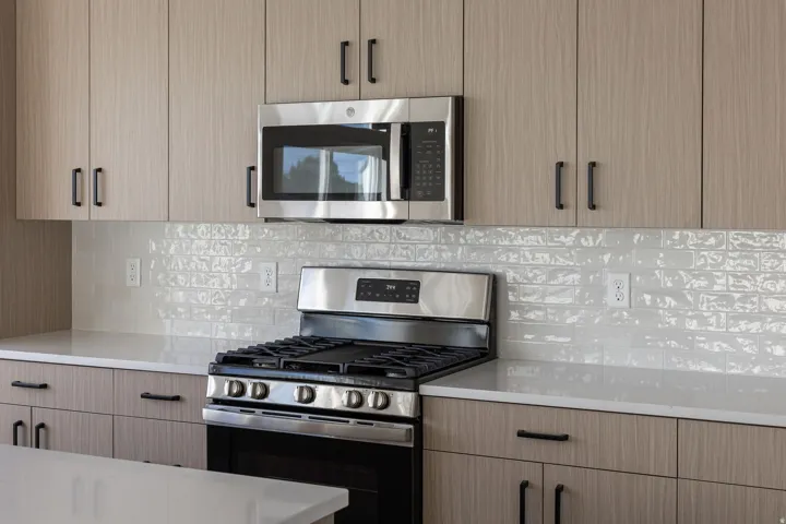 Stainless steel range with a built-in microwave, light wood-finish cabinetry, and a textured subway tile backsplash