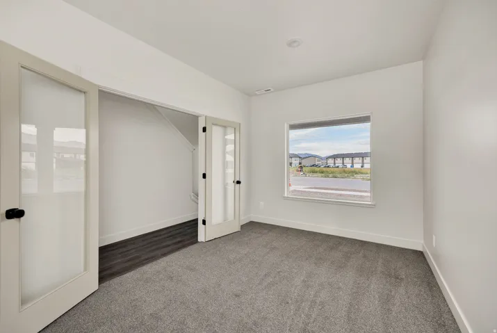 Light gray wall paint, recessed ceiling lighting, gray carpet, double French doors, and a large window