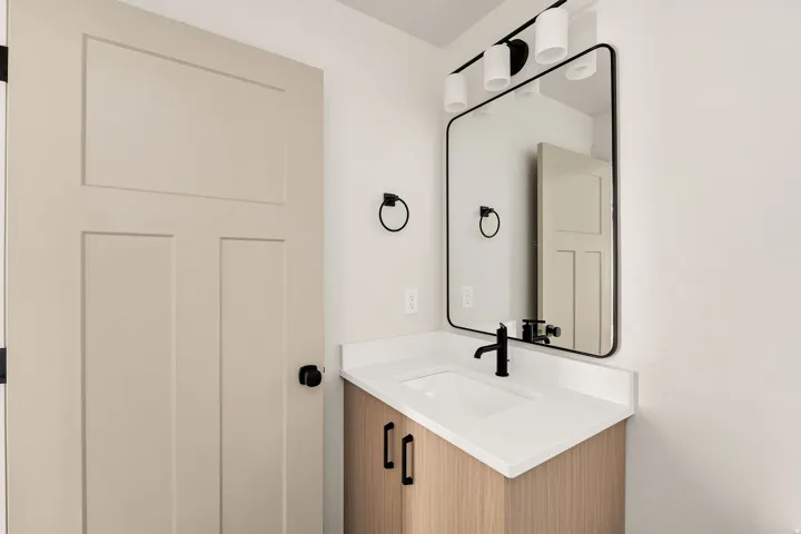 Light wood-finish vanity with a white countertop and integrated sink, matte black faucet, and a contemporary framed mirror