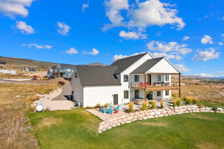 White siding exterior with a dark shingle roof, complemented by an upper-level covered deck, a lower-level patio, and a rock retaining wall