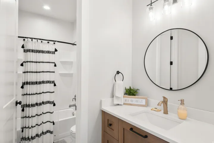 Built-in bathtub with shower, wood-finish vanity with countertop, integrated sink, and wall-mounted light fixture