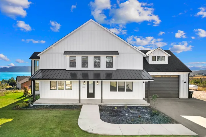 Modern farmhouse exterior with white board and batten siding, black metal roof accents, an integrated garage, and a concrete driveway