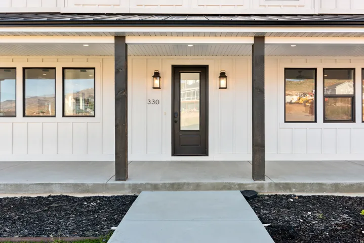 Welcoming front porch featuring a dark entry door with glass pane, board and batten siding, recessed lighting, and black metal roof accent