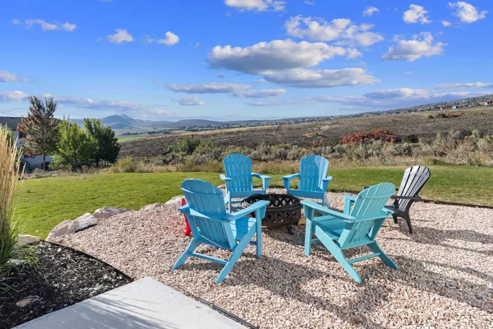 Expansive outdoor space featuring a gravel patio, built-in fire pit, and a grass lawn, with distant mountains