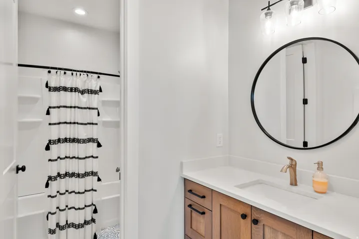 Wood-finish vanity with a white countertop and integrated sink, paired with a round black-framed mirror