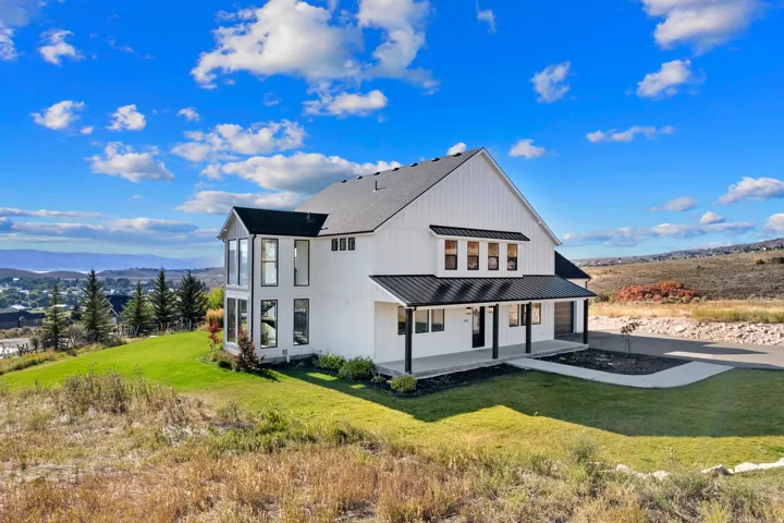 Modern farmhouse exterior with white vertical siding, black-framed windows, dark metal roof accents, covered front porch, and an attached garage