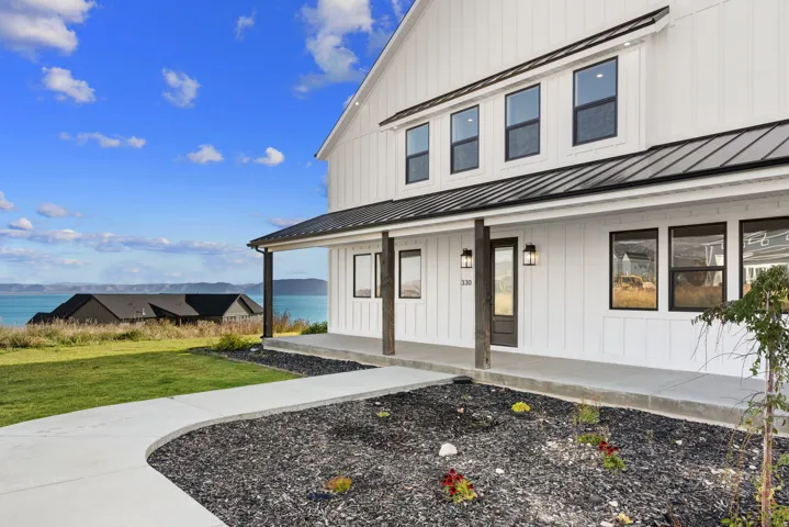 Modern farmhouse exterior featuring board and batten siding, a metal roof, a covered porch with dark wood posts, and a concrete walkway